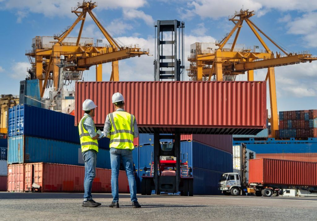 Dos hombres observan grúas portuarias moviendo contenedores de mercancías